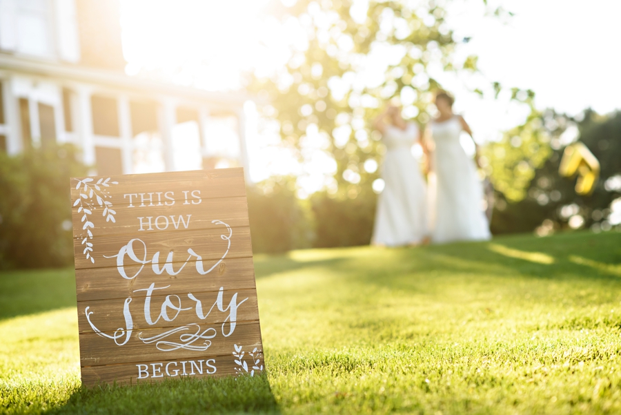 A wooden sign that says our story while a newly married lesbian couple walk in the background.